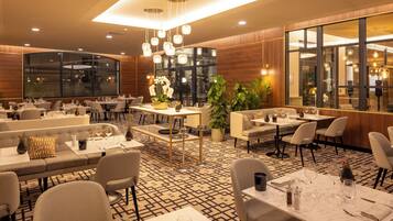 En moderne restaurant med et geometrisk mønstret gulv, flere siddeområder inklusiv borde og båse, samt et stort vindue der giver udsigt over interiøret.