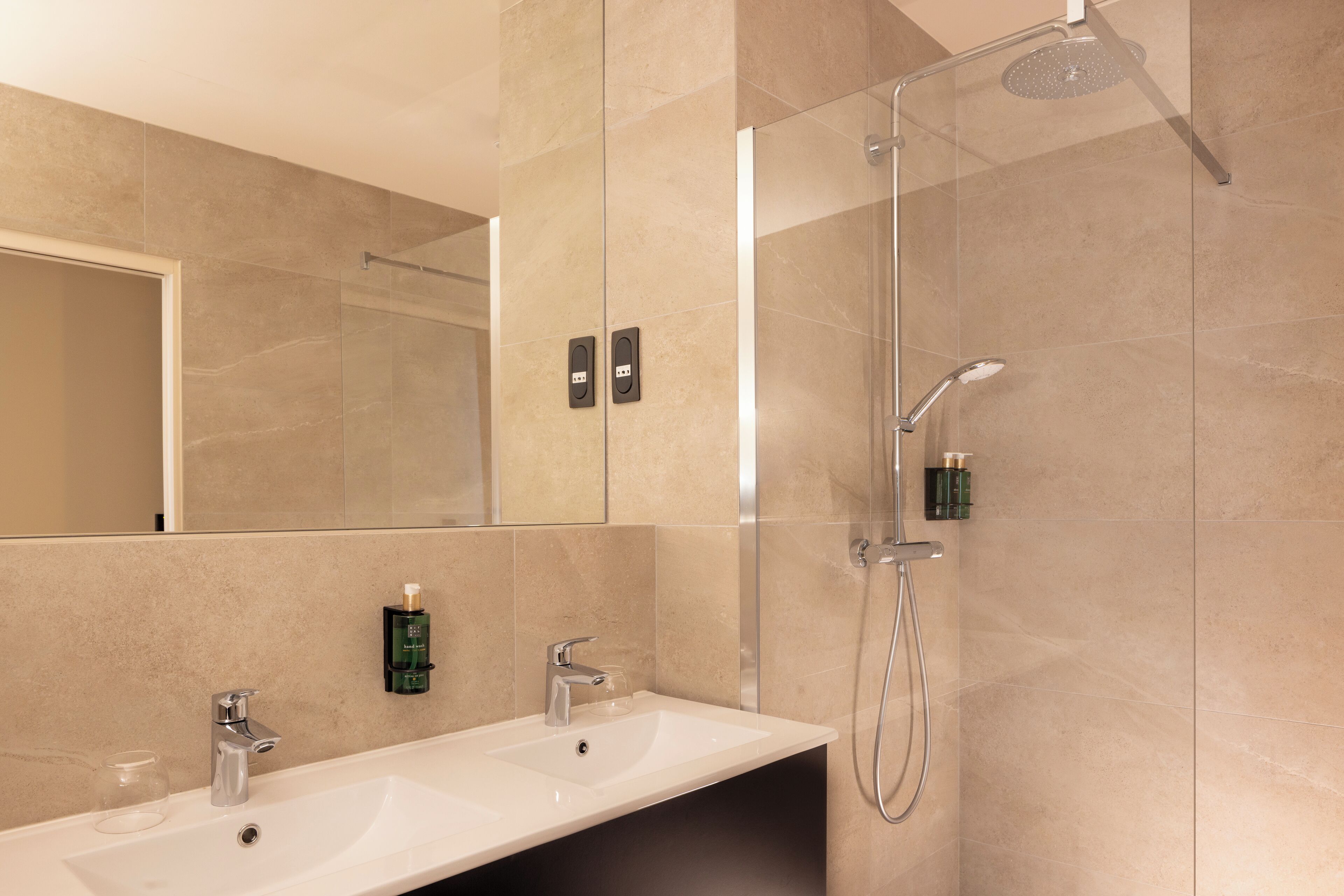 Een moderne badkamer met twee wastafels, een douche en een grote spiegel.