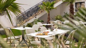 Un restaurante con terraza, mesas blancas, sillas de mimbre y una escalera.