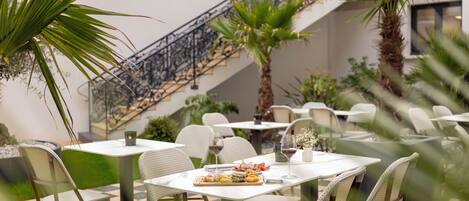 Un restaurante con terraza, mesas blancas, sillas de mimbre y una escalera.