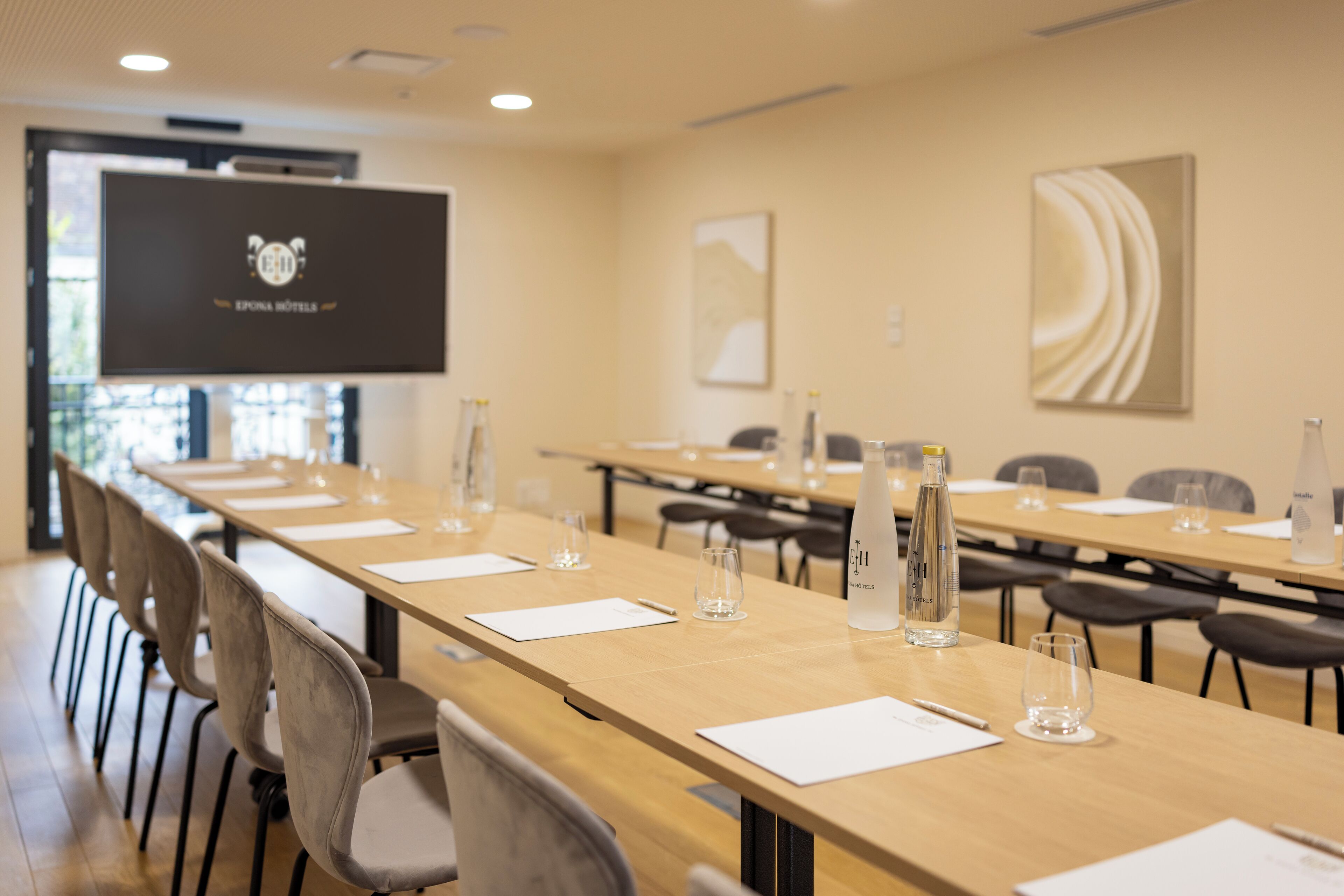 A conference room with long tables, chairs, a projector screen, and a water bottle.