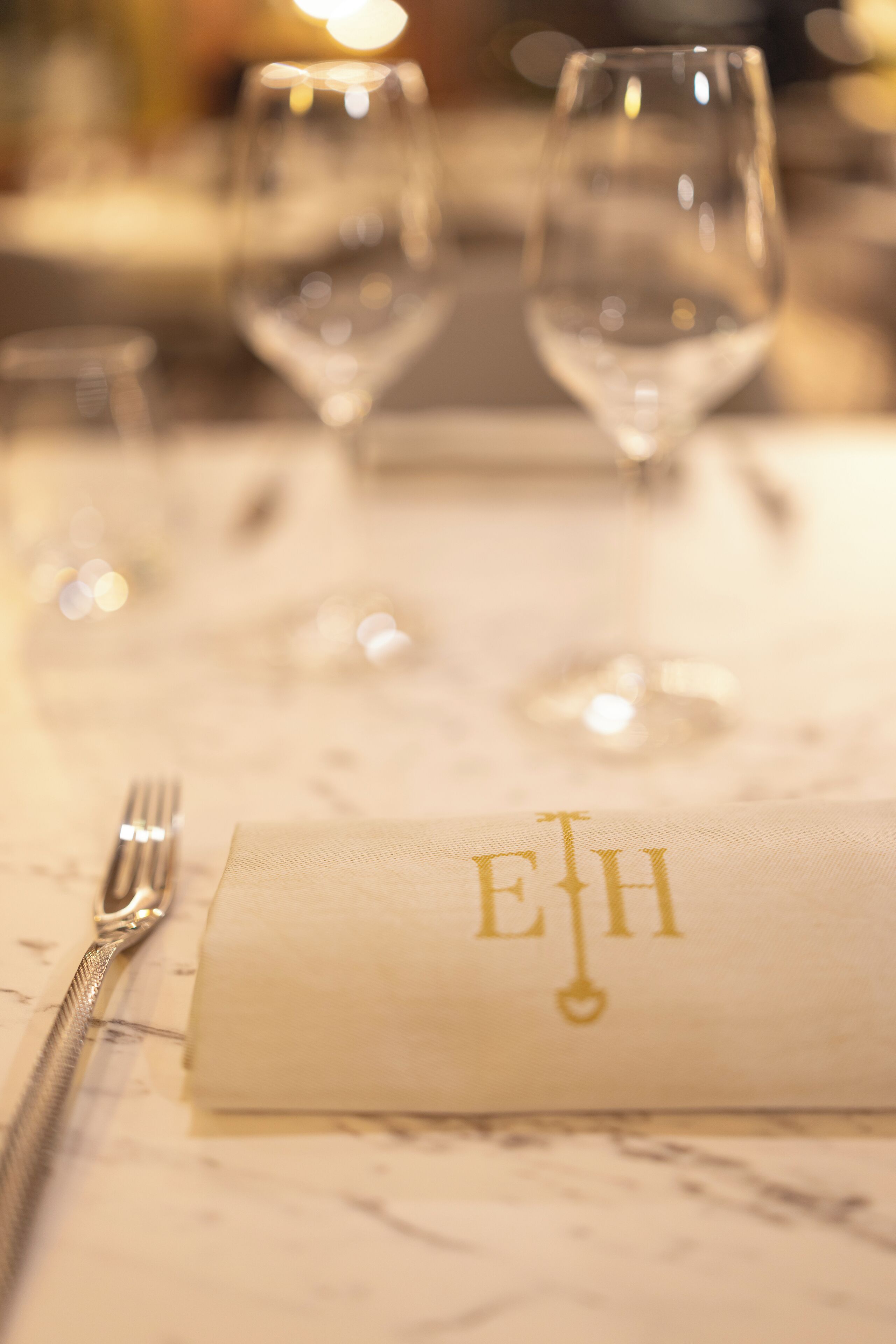 A table setting with a folded napkin featuring a monogram, a fork, and two wine glasses.