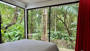 A bedroom with a large bed, a view of a lush garden through a sliding glass door, and a red curtain on the right. - Villa Lapas: Spacious, Lush 2-Bedroom Home & 2-Bedroom Apart, Central, Wildlife! (Quepos)
