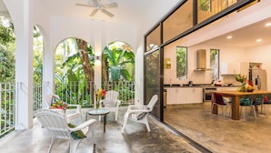 A spacious living area with a view of lush greenery, a modern kitchen, and a dining area with white chairs and a wooden table. - Villa Lapas: Spacious, Lush 2-Bedroom Home & 2-Bedroom Apart, Central, Wildlife! (Quepos)
