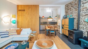 Uma sala de estar moderna com sofá, mesa de centro e área de refeições com cadeiras e mesa. Uma cozinha com fogão e armários é visível ao fundo.