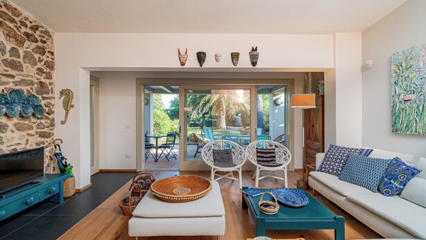 Uma sala de estar moderna com parede de pedra, uma televisão, um sofá e um espaço de jantar com cadeiras e uma mesa.