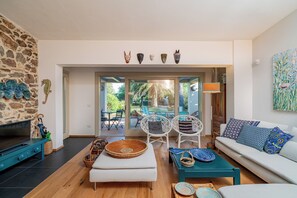 A modern living room with a stone wall, a TV, a sofa, and a dining area with chairs and a table. - Casa Loris by Wonderful Italy (Olbia)