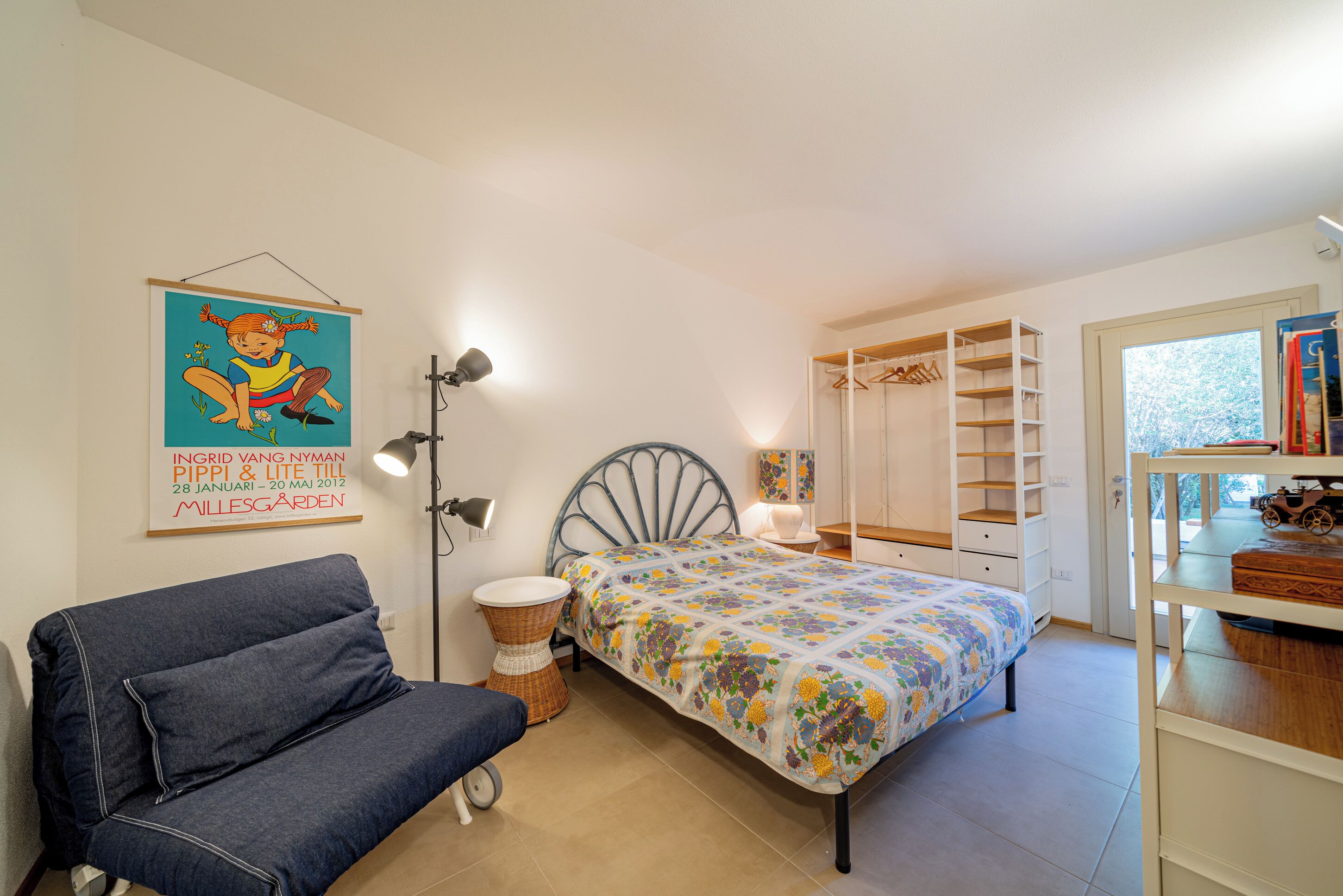 A bedroom with a bed, a sofa, a bedside table, a lamp, a wardrobe, and a window.