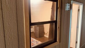 A window with a wooden frame, a white door with a doormat, and a view of a room with a bed and a small table. - Werry'S Cottages And Pub By OYO East Stroudsburg - Weekly Stays (East Stroudsburg)