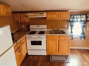 A compact kitchen with a stove, oven, sink, and wooden cabinets. - Werry'S Cottages And Pub By OYO East Stroudsburg - Weekly Stays (East Stroudsburg)