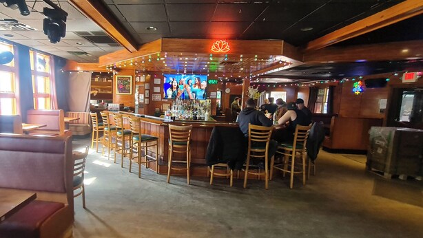 A bar area with wooden chairs and a counter. There are cushioned seating areas and a television screen. - Werry'S Cottages And Pub By OYO East Stroudsburg - Weekly Stays (East Stroudsburg)