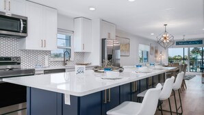 A modern kitchen with white cabinets, a stainless steel refrigerator, and a large island with bar stools.
