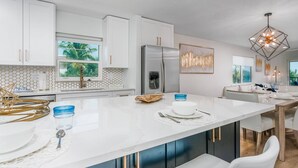 A modern kitchen with white cabinets, a large island, and a stainless steel refrigerator.