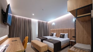 A modern hotel room with two beds, a desk, a chair, and a TV mounted on the wall. - Hotel Dior (Krujë)