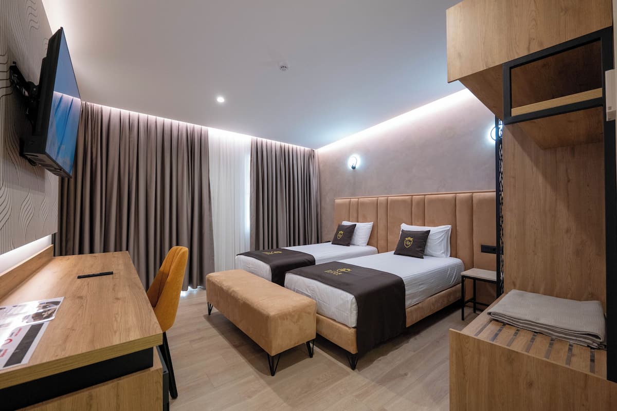 A modern hotel room with two beds, a desk, a chair, and a TV mounted on the wall.