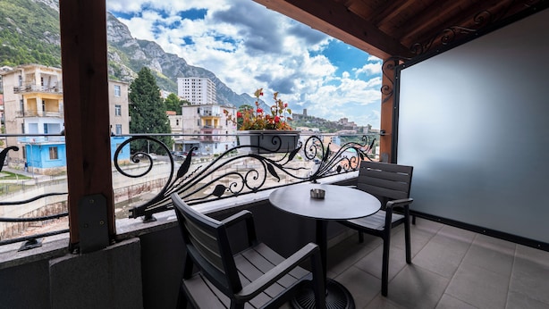 A balcony with a table and chairs, overlooking a cityscape with buildings and mountains. - Hotel Dior (Krujë)