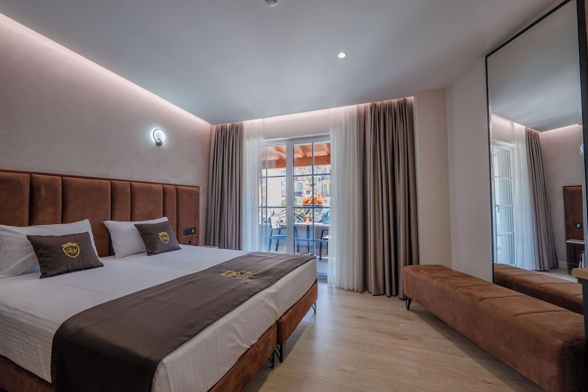 A modern hotel room with a large bed, a bench, and a view of the outside.