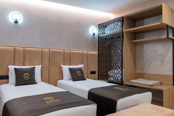 A hotel room with two beds, each with a headboard and pillows, a wooden shelf unit, and two wall-mounted lights. - Hotel Dior (Krujë)