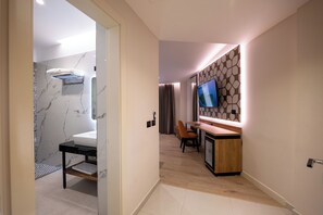 A modern hotel room with a marble bathroom, a wooden dining area, and a TV mounted on the wall.