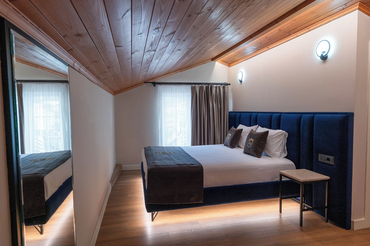 A bedroom with a bed, a bedside table, a mirror, and a window with curtains.