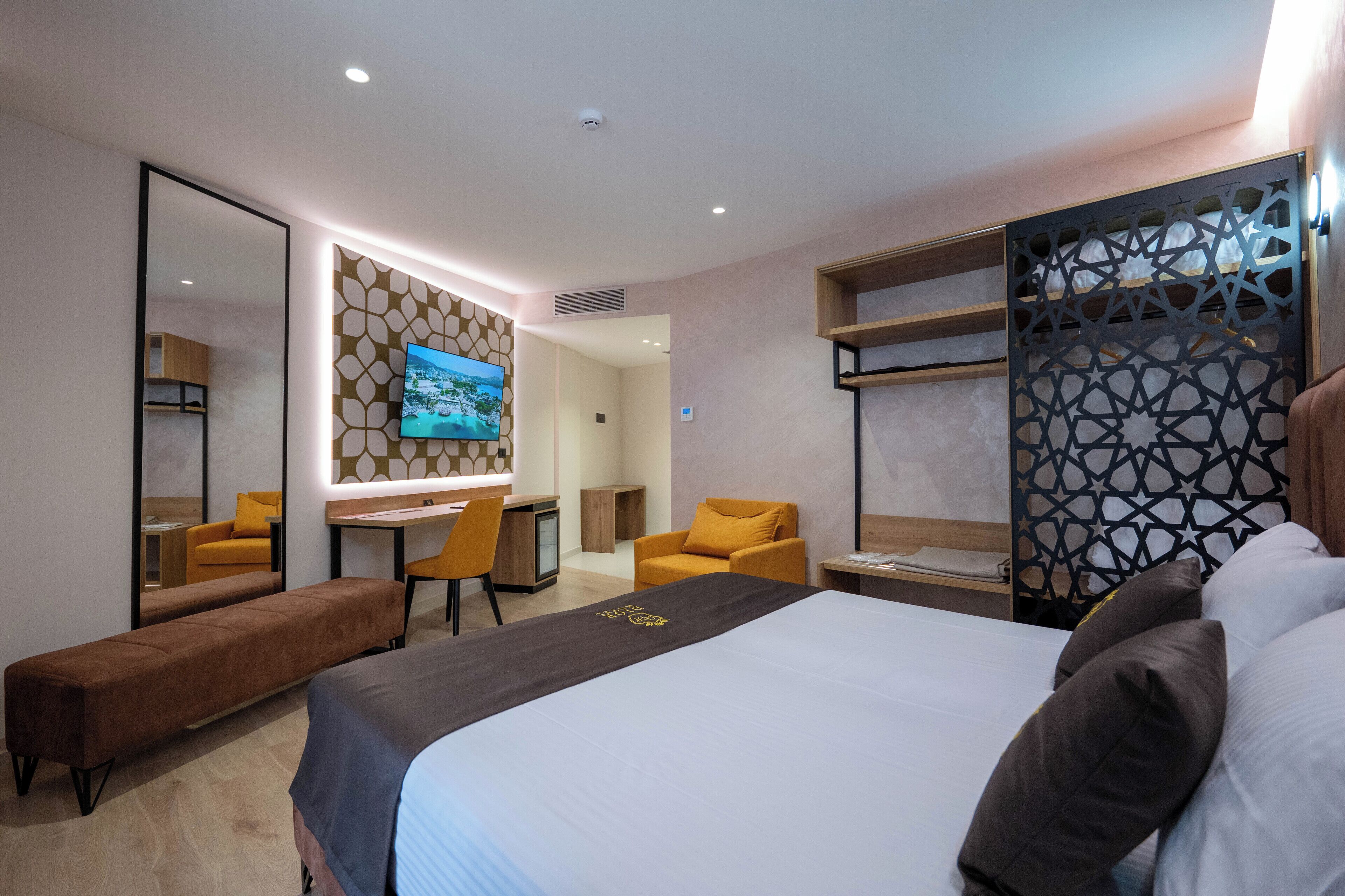 A modern hotel room with a large bed, a desk, a chair, and a bench.