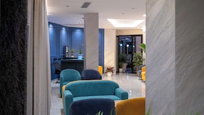 A modern hotel lobby with a marble reception desk, teal and yellow seating, and a large potted plant. - Hotel Dior (Krujë)