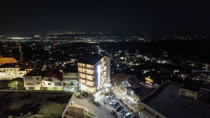 A multi-story hotel with a parking area in front, surrounded by residential buildings and a cityscape at night. - Hotel Dior (Krujë)