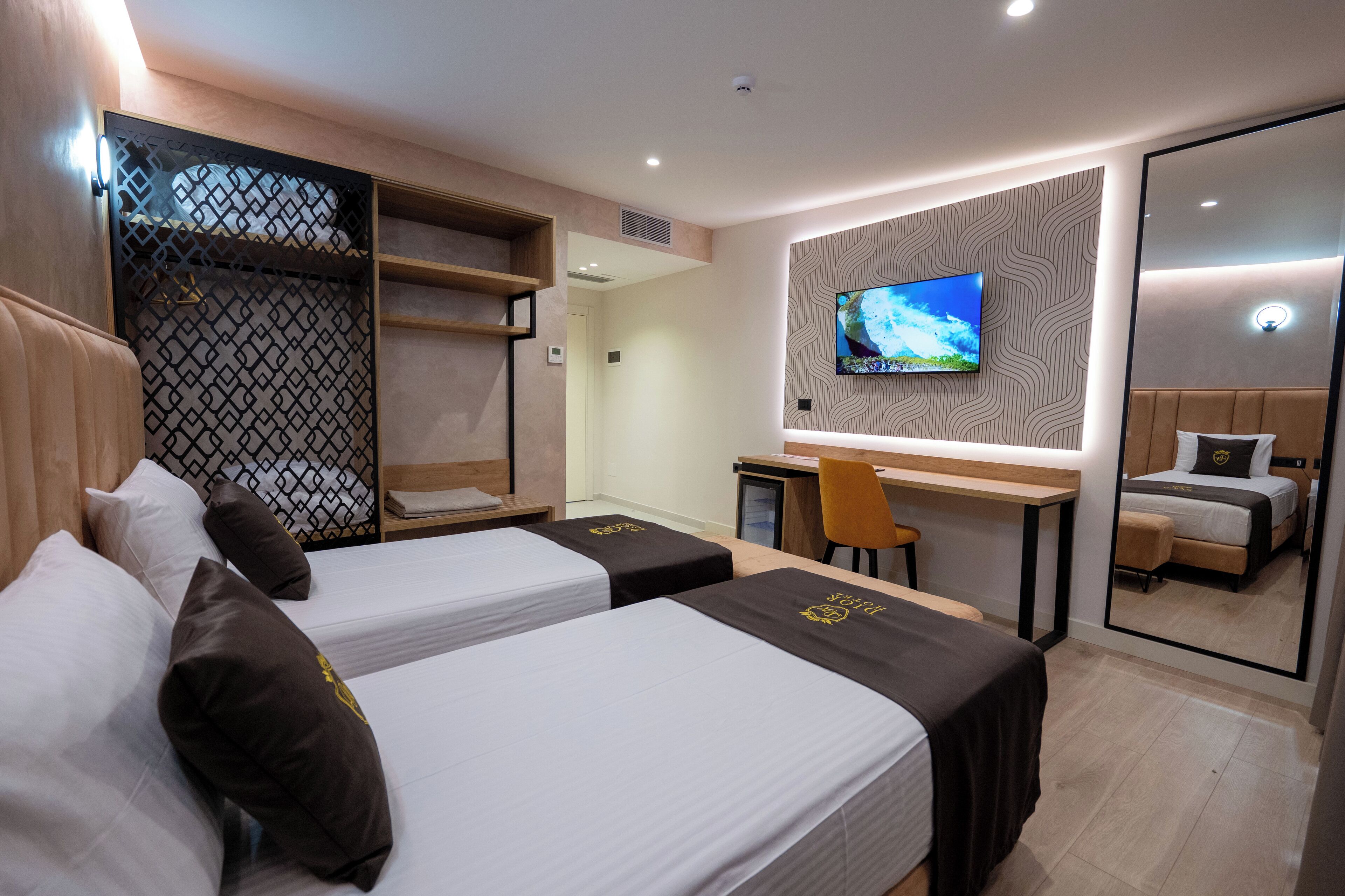 A hotel room with two beds, a desk, a TV, and a mirror.