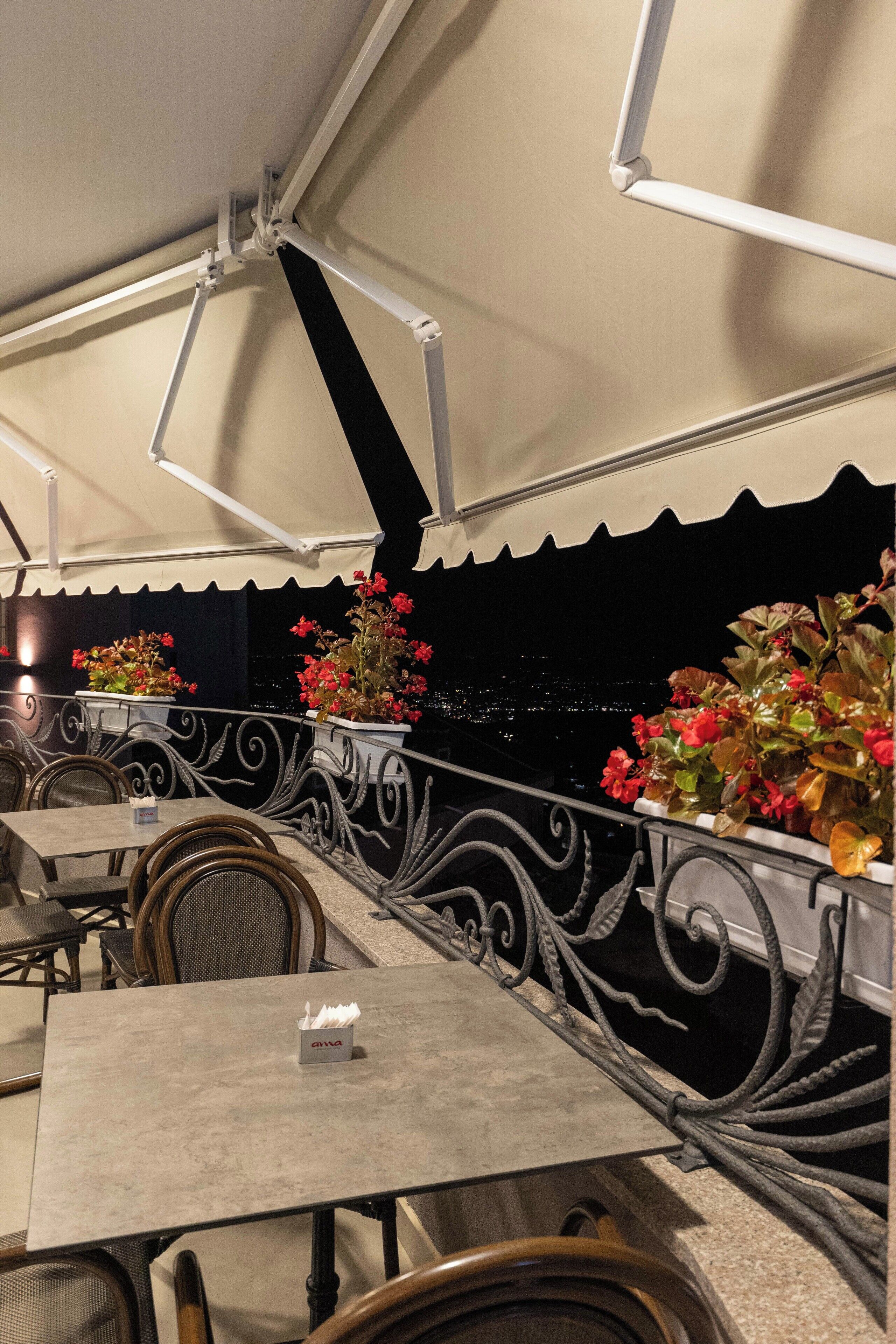 An outdoor dining area with tables and chairs, a railing with decorative elements, and potted plants.