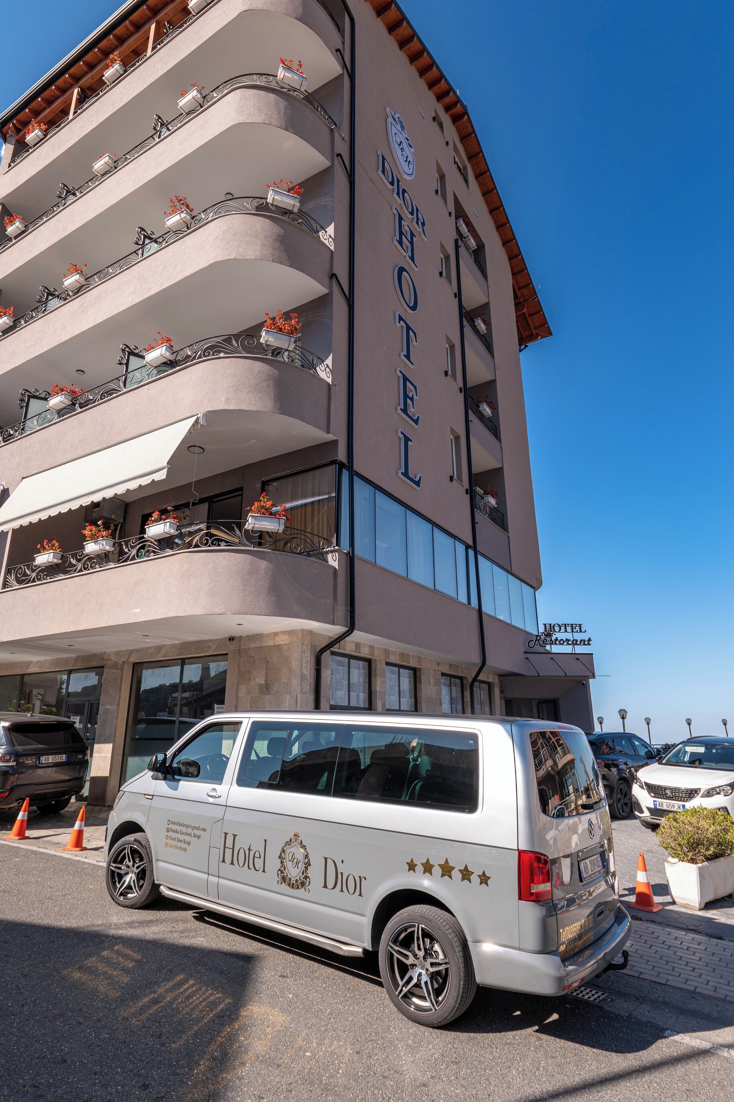 Un edificio de hotel de varios pisos con balcones, una furgoneta estacionada y un cielo azul despejado.