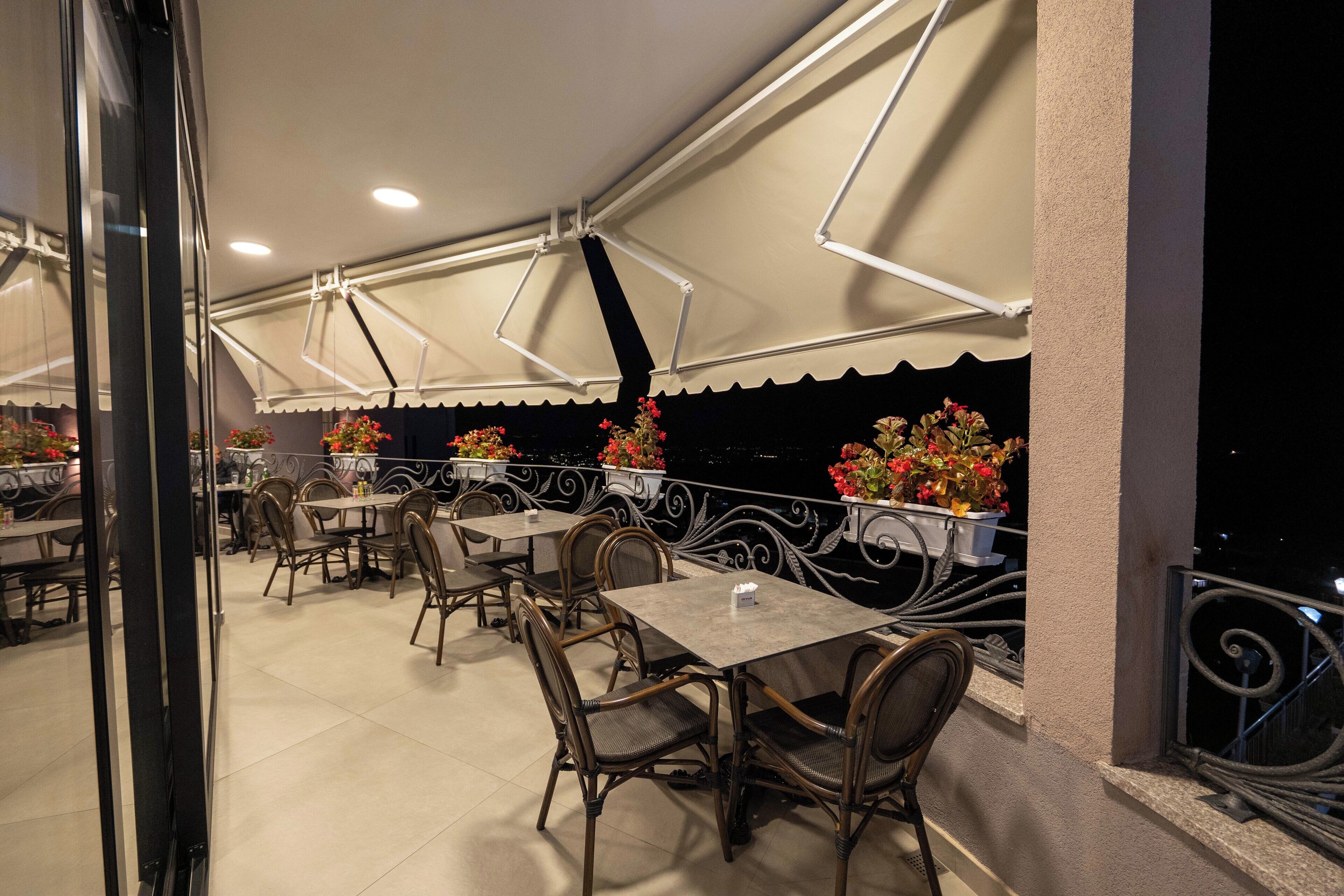 An outdoor patio with tables and chairs, a railing, and potted plants.