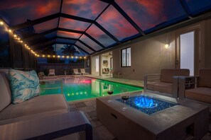 Un espace piscine doté d’un toit en verre, de chaises longues et d’un foyer.