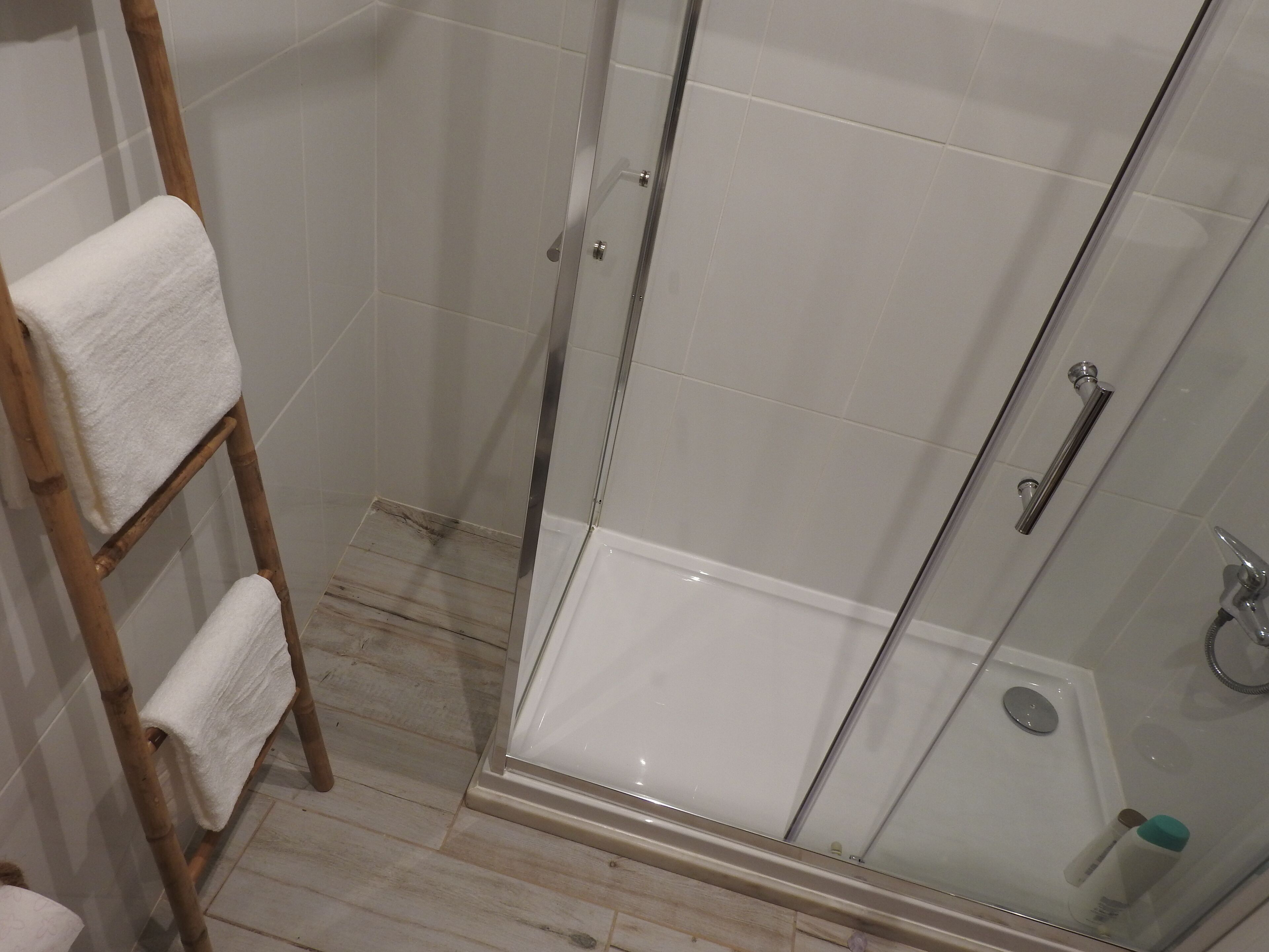 Een douche met glazen wanden, een houten handdoekhouder en een vloer van witte tegels.
