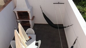 A patio with a white table, chairs, a hammock, and a barbecue grill. - Seacastle Residence Peniche (Atouguia da Baleia)