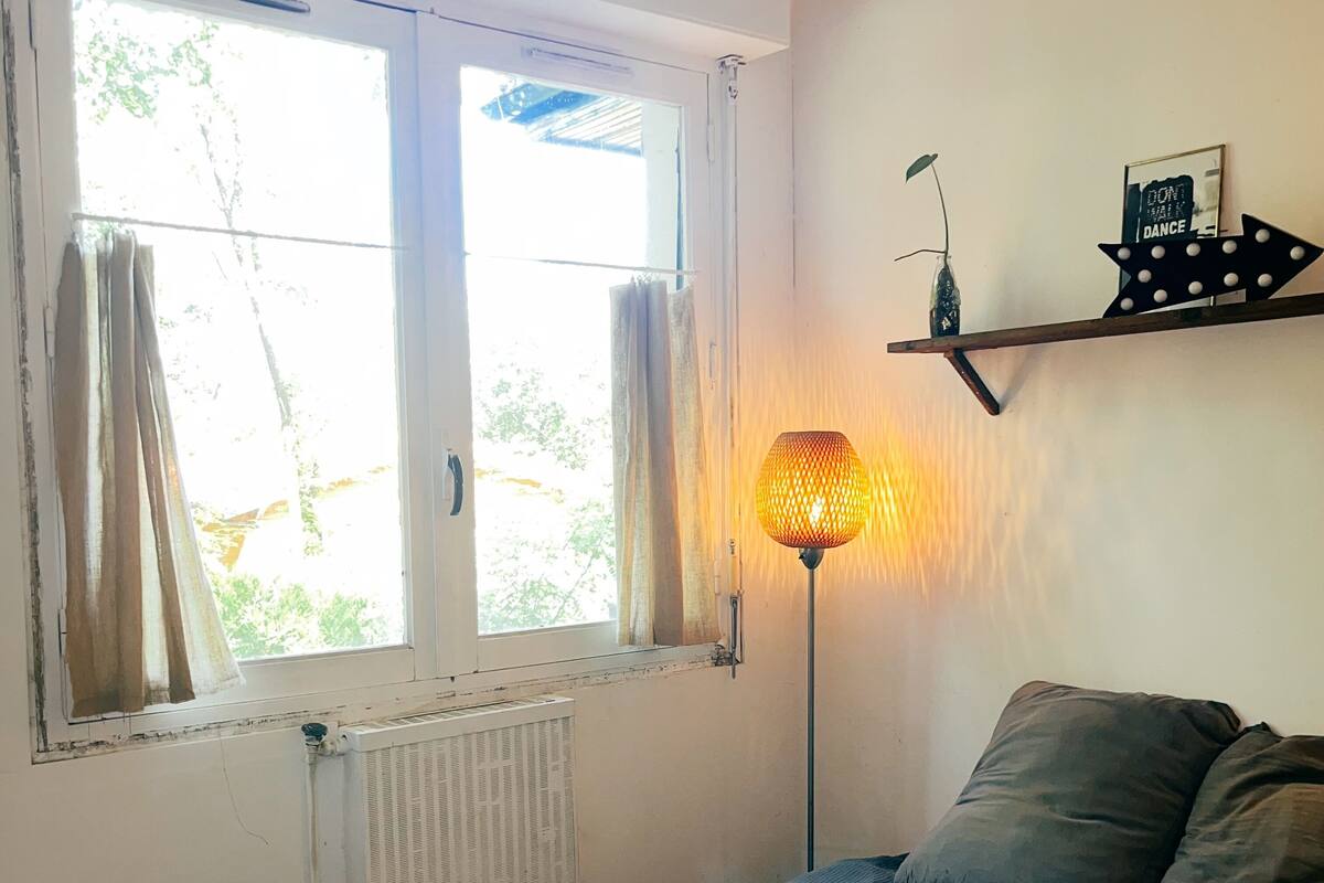 Un dormitorio con cama, un radiador, una ventana con cortinas y un estante de pared con un objeto decorativo.