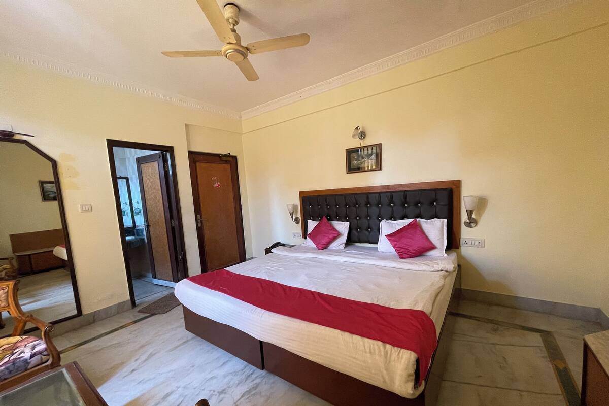 A hotel room with a bed, a ceiling fan, a wooden door, and a small table with a chair.