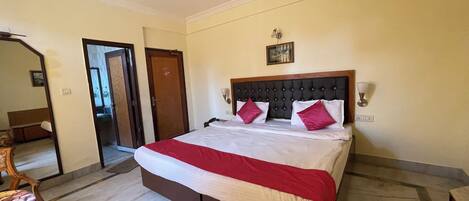 A hotel room with a bed, a ceiling fan, a wooden door, and a small table with a chair.