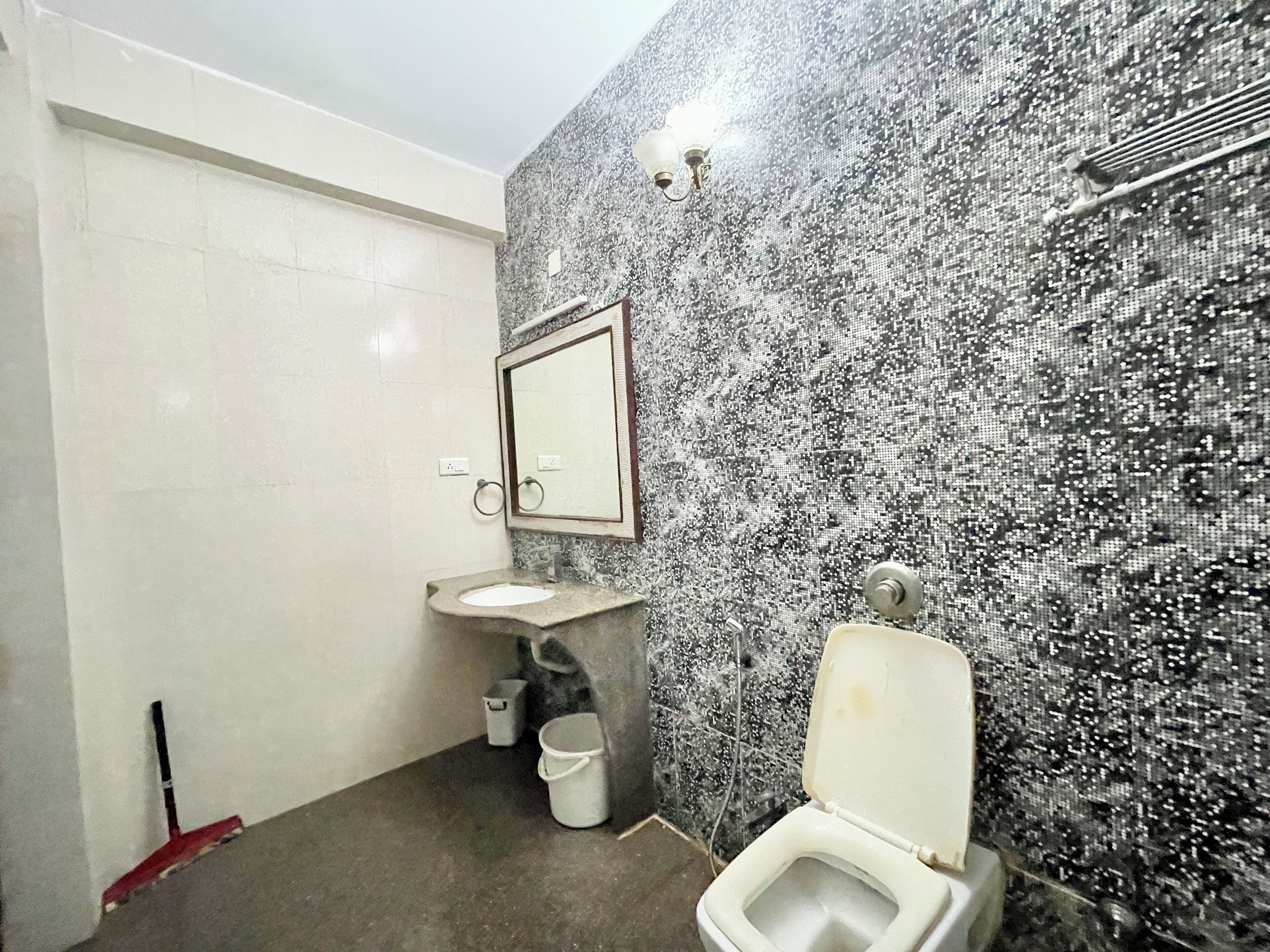 A bathroom with a marble wall, a sink, a toilet, and a mop leaning against the wall.