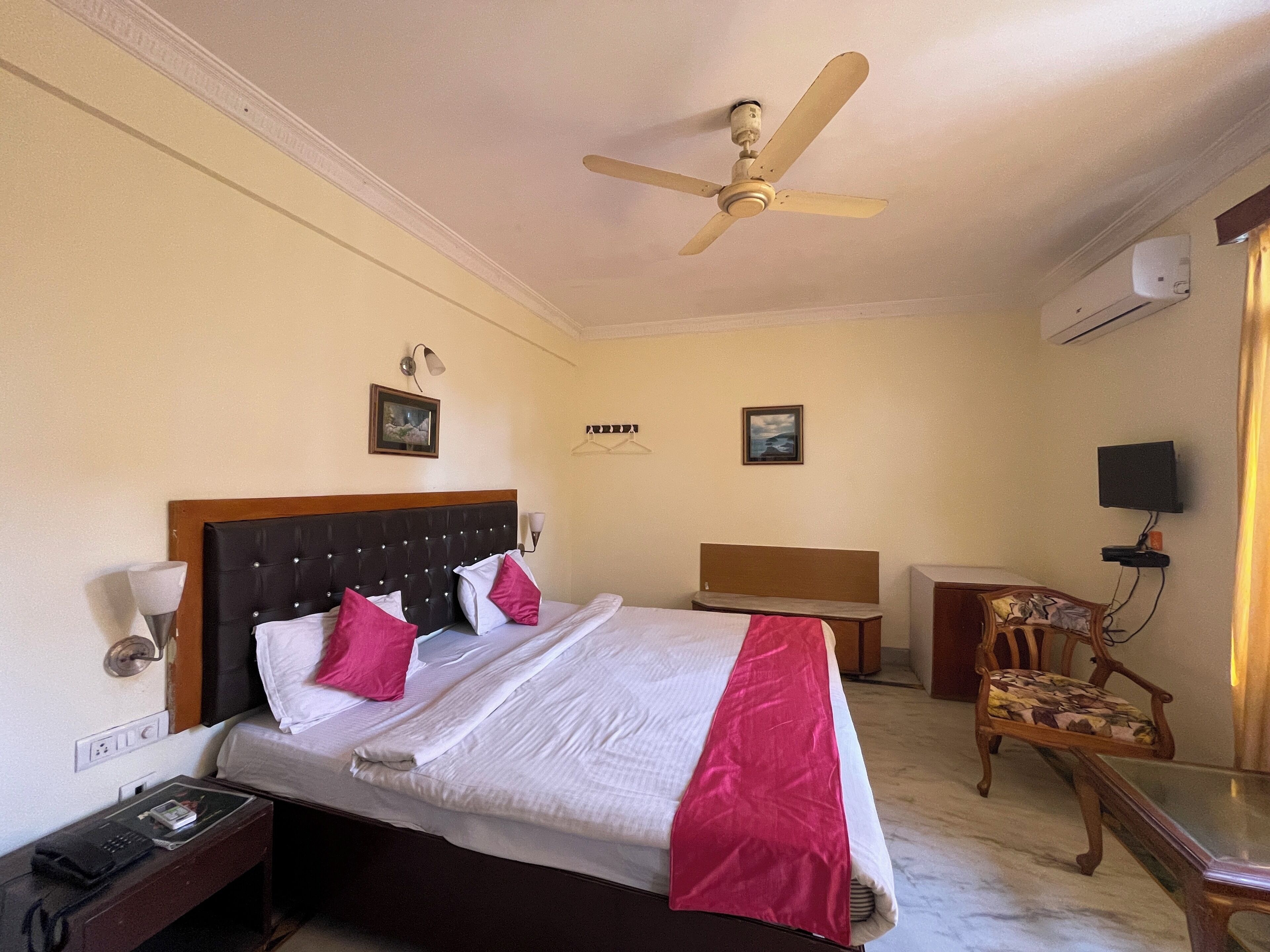 A hotel room with a bed, a desk, a chair, a ceiling fan, and an air conditioning unit.