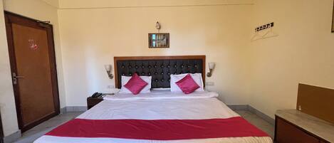 Habitación de hotel con una cama grande, cabecera de madera, dos lámparas de noche, ventilador de techo y una puerta.