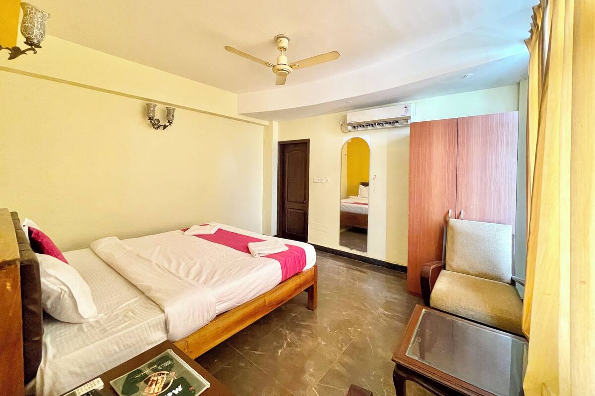 A hotel room with a bed, a chair, a table, a ceiling fan, and an air conditioning unit.
