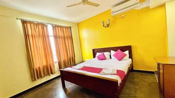 Habitación de hotel con cama, cortinas, ventilador de techo y aire acondicionado.