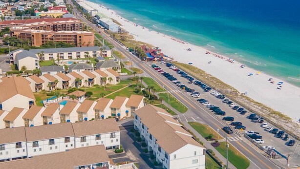 Un hotel frente al mar con edificios de varios pisos, estacionamiento y vistas a la playa.