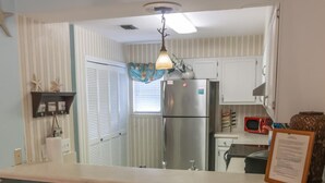 Una cocina con un refrigerador de acero inoxidable, un microondas y un lavamanos. Hay dos sillas de mimbre frente a la encimera.
