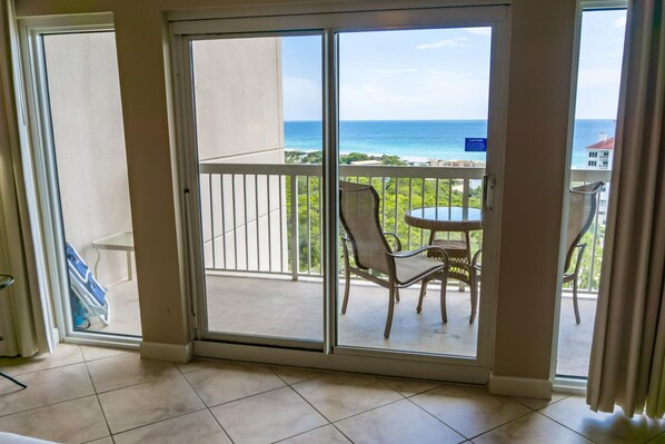 A room with a sliding glass door leading to a balcony with a view of the ocean.