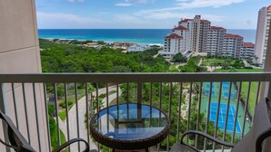 A balcony with a glass table, overlooking a tennis court and a beachfront hotel. - Summit at Topsail 1011 - 10th Floor (Miramar Beach)