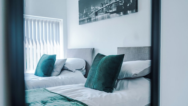 A hotel room with two beds, white bedding, and a cityscape photo on the wall. - Salford Oasis Retreat (Salford)