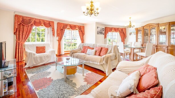 Un salon spacieux comprenant un canapé, des fauteuils, une table basse en verre et un coin repas avec des chaises et un buffet.