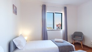 Ett hotellrum med två sängar, en stol, ett fönster med gardiner och utsikt över byggnaderna utanför.