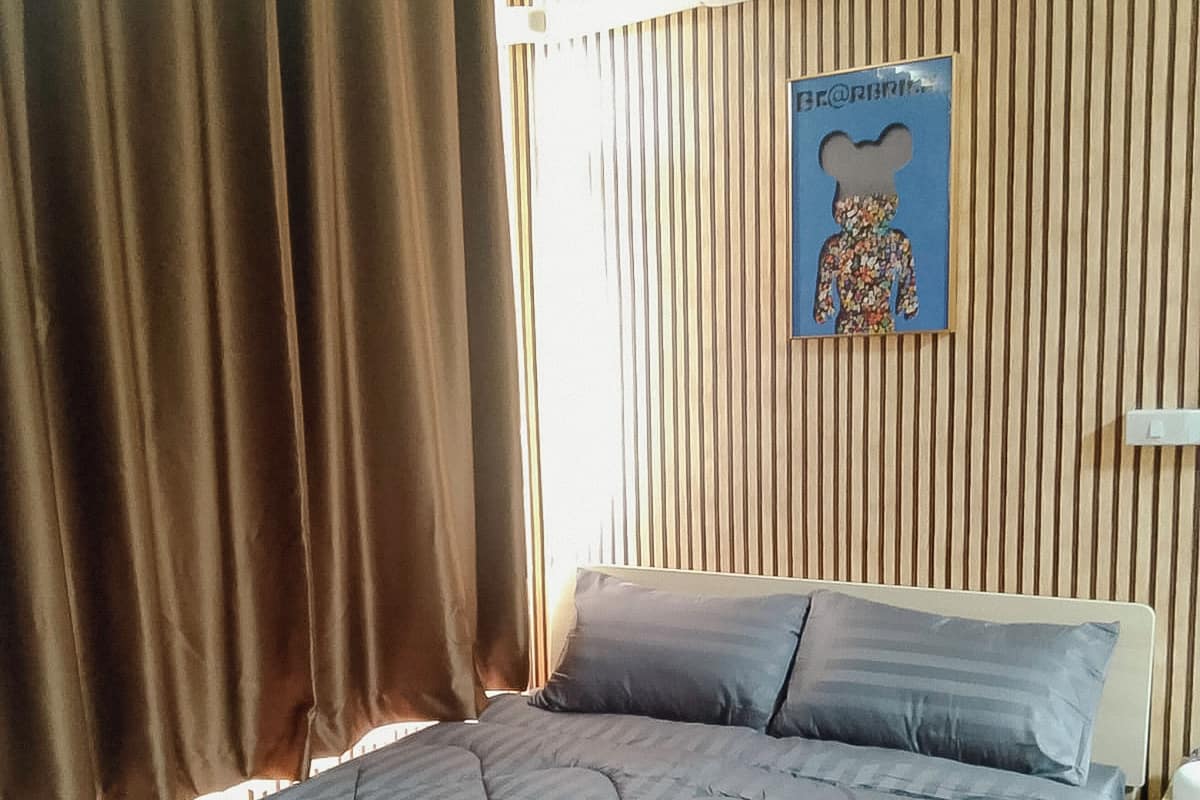 A bedroom with a bed, curtains, an air conditioning unit, and a wall-mounted poster.